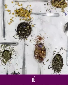 MycoVital_ Una variedad de tés y hierbas secas de hoja suelta presentados en cucharas de plata, dispuestos sobre una superficie de mármol blanco. La palabra TEE aparece en un rótulo morado en la parte inferior.