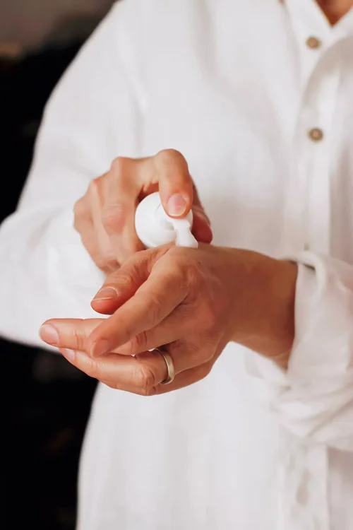MycoVital_ A person wearing a white shirt applies lotion or sanitizer from a pump bottle onto the back of their hand. The person has a ring on their left ring finger.