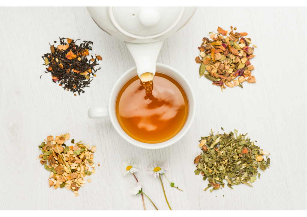 MycoVital_ Eine Teekanne gießt Tee in eine weiße Tasse, umgeben von vier Stapeln loser Teemischungen und zwei kleinen Kamillenblüten auf einer hellen Holzfläche.